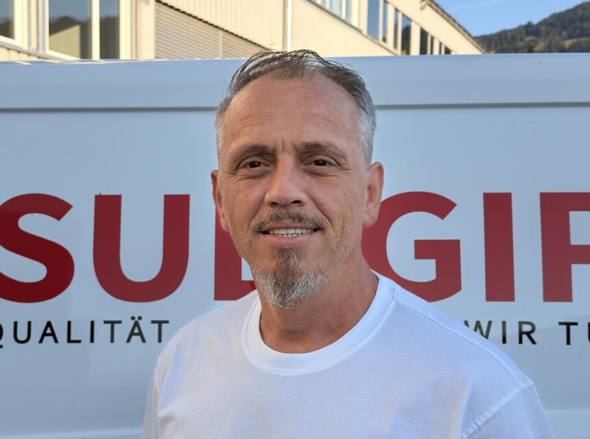 Man in white Sulgips t-shirt standing in front of a white van with red Sulgips branding and logo, office building in background.